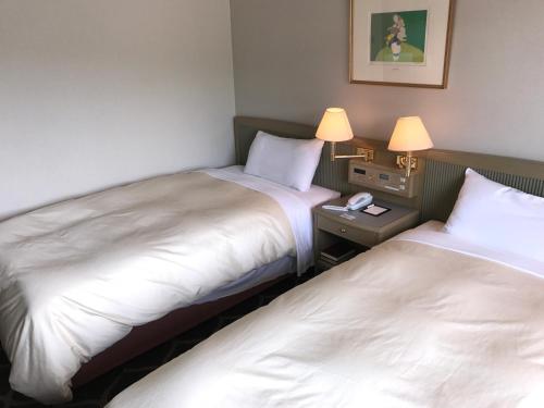two beds in a hotel room with two lamps at Hotel Grand Terrace Chitose in Chitose
