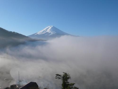 a mountain shrouded in fog with a tree in the foreground at Mizno Hotel in Fujikawaguchiko