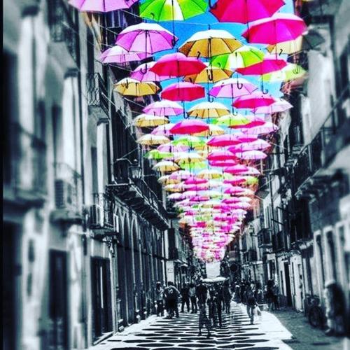 a row of colorful umbrellas hanging over a street at B&B Quintino Sella in Iglesias