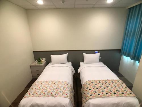 two beds in a small room with blue curtains at Chang Ti Metropolis Commercial Hotel in Zhongli