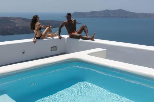 two people sitting on the back of a boat next to a swimming pool at Aria Suites & Villas in Fira