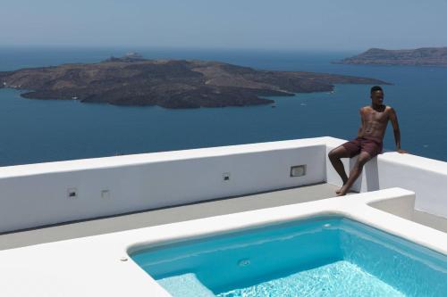a man sitting on the edge of a house with a swimming pool at Aria Suites & Villas in Fira