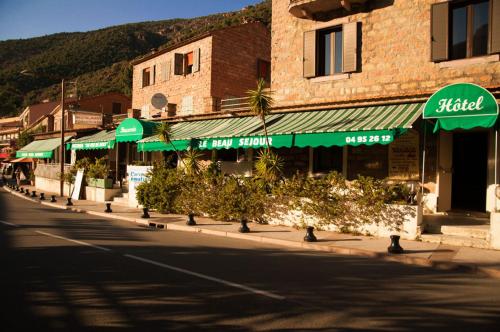 a street with a building with green umbrellas at Hotel & Restaurant Le Beau Sejour in Porto Ota