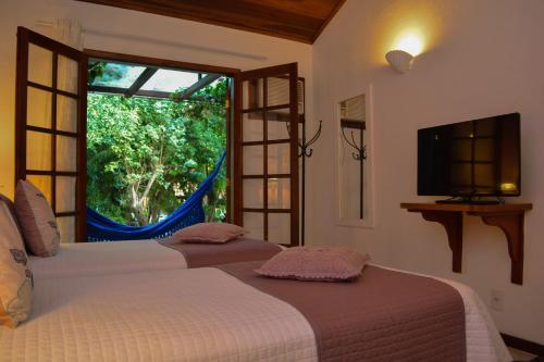 two beds in a room with a window and a tv at Pousada do Namorado in Búzios