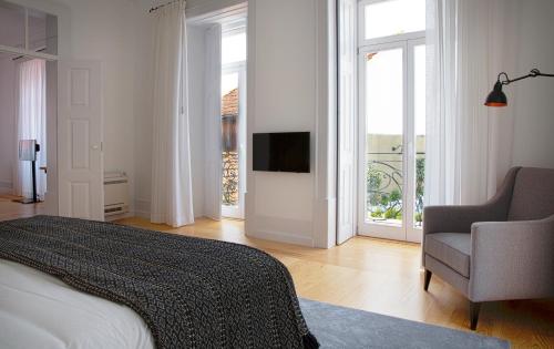 a bedroom with a bed and a chair and windows at Sapientia Boutique Hotel in Coimbra