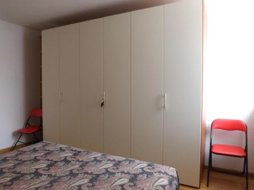 カヴァレーノにあるAppartamento a Cavareno Val di Nonの白いキャビネットと赤い椅子が備わるベッドルーム1室