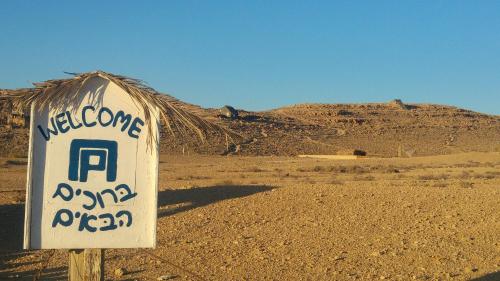 a sign in the middle of a desert with a mountain at Succah in the Desert in Mitzpe Ramon