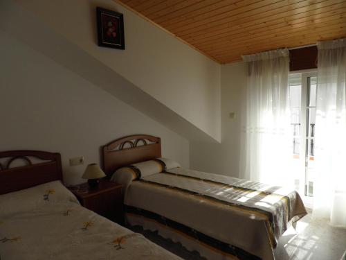 a bedroom with two beds and a window with curtains at Novas Foxos (Ático) in A Lanzada