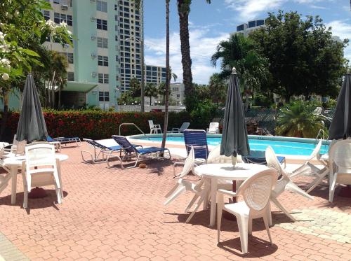 eine Gruppe von Tischen und Stühlen mit Sonnenschirmen neben einem Pool in der Unterkunft Birch Patio Motel in Fort Lauderdale