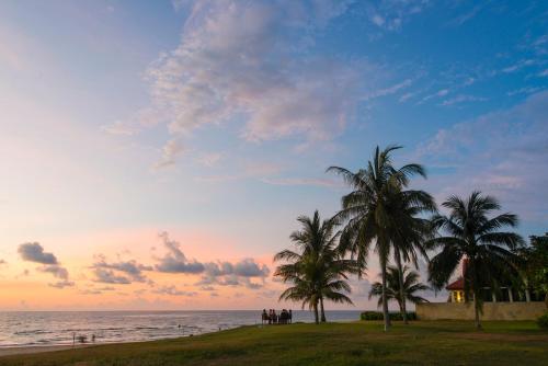 a group of people standing under palm trees on the beach at Sabah Beach Villas & Suites in Kota Kinabalu