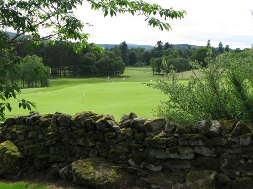 a stone wall in front of a golf course at Apartment 20 Inchmarlo in Banchory