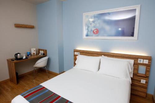 a bedroom with a white bed and a desk with a chair at Travelodge Valencia Aeropuerto in Manises