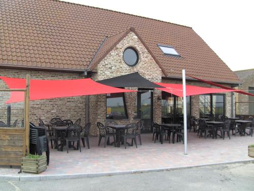 un patio avec des tables, des chaises et des parasols rouges dans l'établissement 't Vossenerf, au Coq