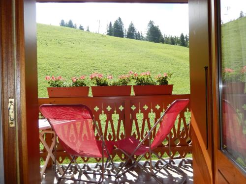 d'une chaise rouge et d'une table fleurie sur le balcon. dans l'établissement La Vieille Ferme, à Manigod