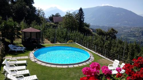 a swimming pool in a yard with chairs and mountains at Zimmervermietung Gröberhof in Schenna