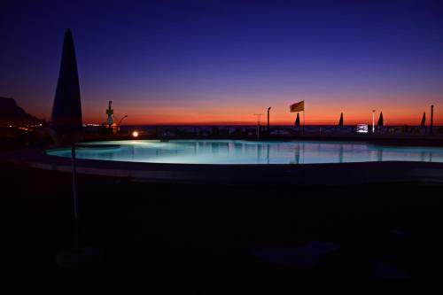 a large swimming pool with a sunset in the background at Saracen Sands Hotel & Congress Centre - Palermo in Isola delle Femmine