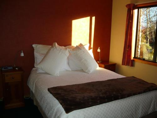 ein Schlafzimmer mit einem Bett mit weißen Kissen und einem Fenster in der Unterkunft Birchwood Cottages in Te Anau