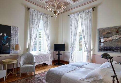 a bedroom with a bed and a chandelier and two windows at Hotel Ploes in Ermoupoli