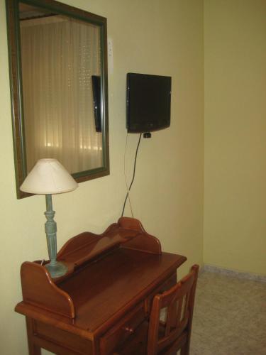 a desk with a lamp and a television on a wall at Hostal El Pinar in Avila