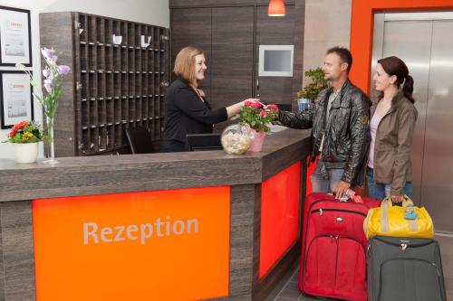 a group of people standing at a reception counter with luggage at Ringhotel Alfsee Piazza in Rieste