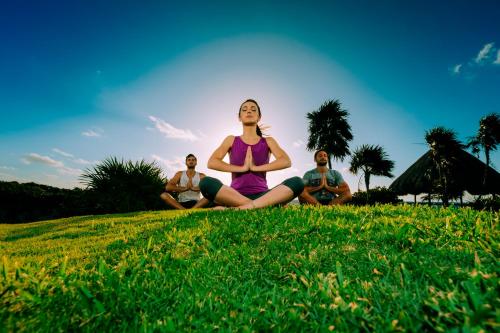 a group of three women sitting in a field doing yoga at Occidental at Xcaret Destination - All Inclusive in Playa del Carmen