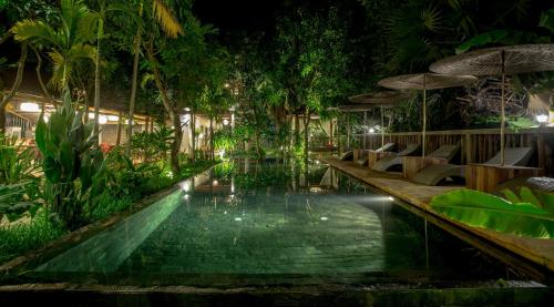 暹粒的住宿－伊桑別墅，夜间在度假村的游泳池,配有椅子和遮阳伞
