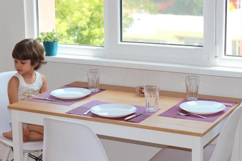 een klein meisje zit aan een tafel met borden bij Apartment 17 in Velingrad
