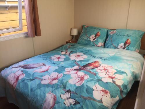 ein Bett mit einer blauen Bettdecke mit Vögeln und Blumen in der Unterkunft Stacaravan Jade in IJmuiden