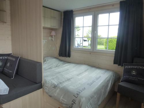 a small bed in a small room with a window at zeeuwse chalet voor 2 personen in Serooskerke