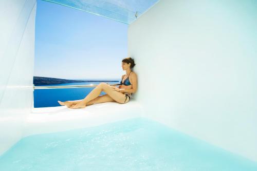 a woman sitting on a ledge next to the water at Hyperion Oia Suites in Oia