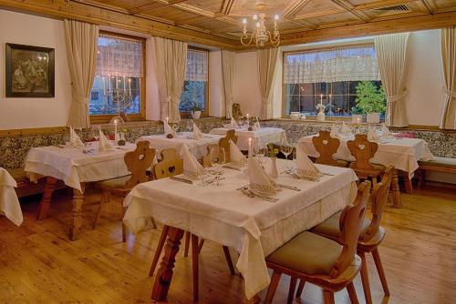 un comedor con mesas y sillas blancas y ventanas en Hotel Gissbach, en Brunico