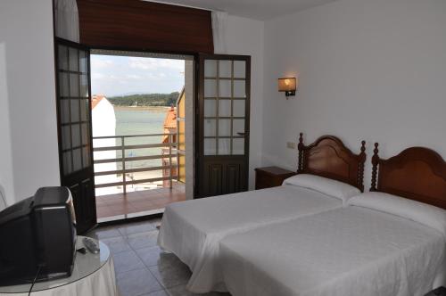 1 dormitorio con cama, TV y balcón en Hostal Mourelos, en O Grove