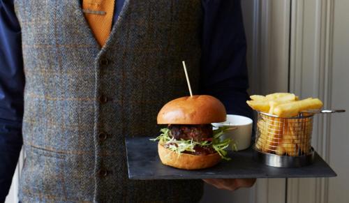 a man holding a tray with a sandwich and chips at The Roseate Edinburgh - Small Luxury Hotels of the World in Edinburgh