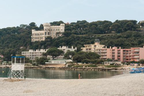 a person standing on a beach with buildings in the background at Hôtel Alexandra in Roquebrune-Cap-Martin