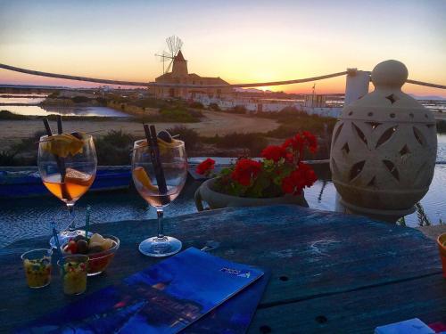 a table with two glasses of wine on it with the sunset at The blue house in Marsala