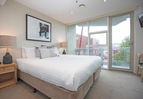 a bedroom with a large bed and a balcony at Sullivans Cove Apartments in Hobart