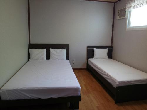 two beds in a room with white sheets and a window at Sorak Garden Resortel in Sokcho