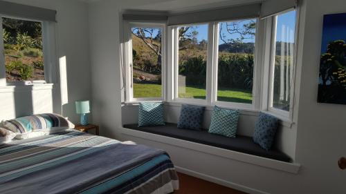 a bedroom with a bed and two windows with pillows at Hot Water Beach Surf Sound Cottage in Hotwater Beach