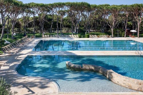 a large swimming pool with blue water and trees at Riva Del Sole Resort & SPA in Castiglione della Pescaia