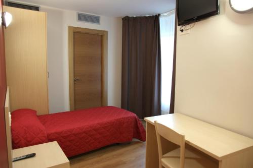 Habitación pequeña con cama roja y mesa. en Hostal Santel San Marcos en Salamanca