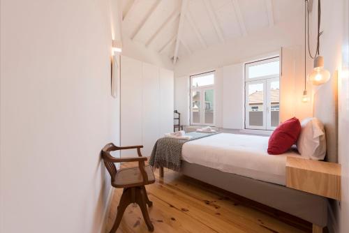 a bedroom with a bed and a chair and two windows at LovelyStay - Top Floor Balcony Apartment in Porto