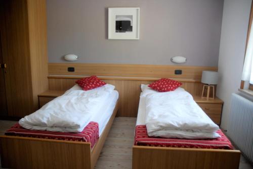 two beds in a small room with red and white pillows at Ciasa Alpina Relax Hotel in Moena