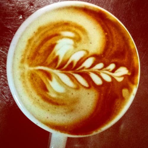 a cup of coffee with a leaf painted on it at Cabin Resort in Moshav Ramot