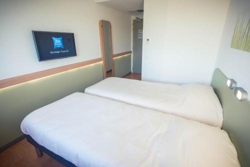 two beds in a room with a tv on the wall at ibis budget Troyes Est in Saint-Parres-aux-Tertres
