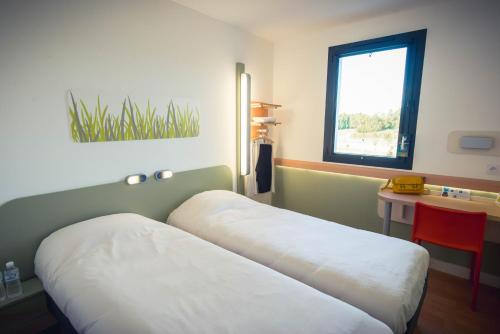 a room with two beds and a table and a window at ibis budget Troyes Est in Saint-Parres-aux-Tertres
