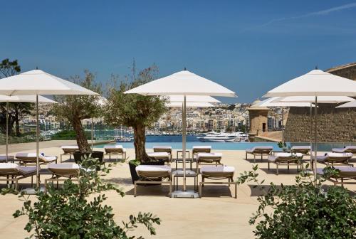 un patio con sillas y sombrillas junto a una piscina en The Phoenicia Malta en La Valeta