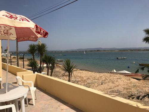 a beach with a table and an umbrella and the water at Apartamentos Barracuda in Faro