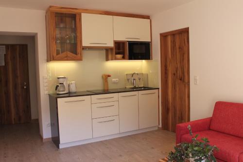 a kitchen with white cabinets and a red couch at Pension Baumgarten in Naturno