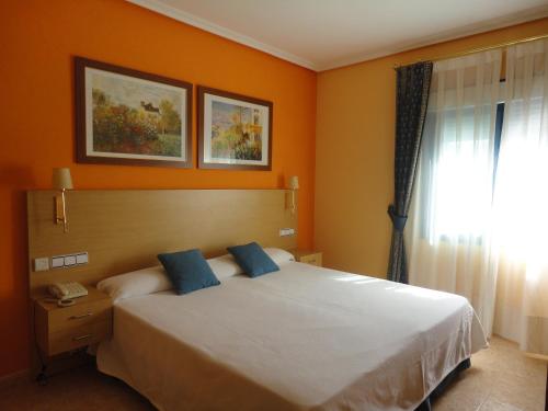 1 dormitorio con 1 cama con paredes de color naranja y ventana en Hotel Mirador, en Velilla de San Antonio