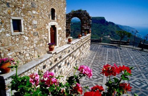 a stone building with flowers in front of it at Mare Blu in Gioiosa Marea